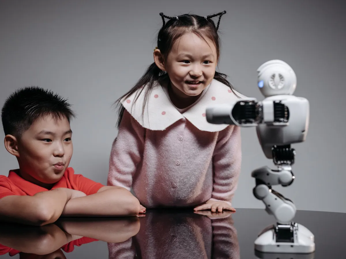 Smiling girl and boy interacting with a small humanoid robot on a table