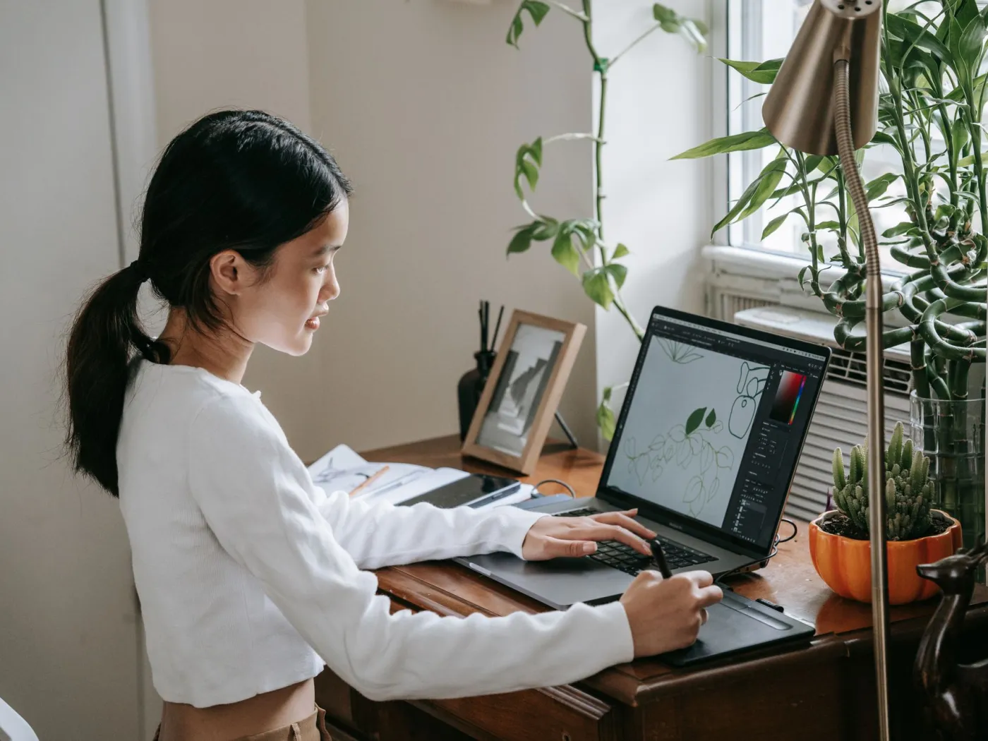 A student uses a pen tablet to create a digital plant illustration shown on her laptop screen.