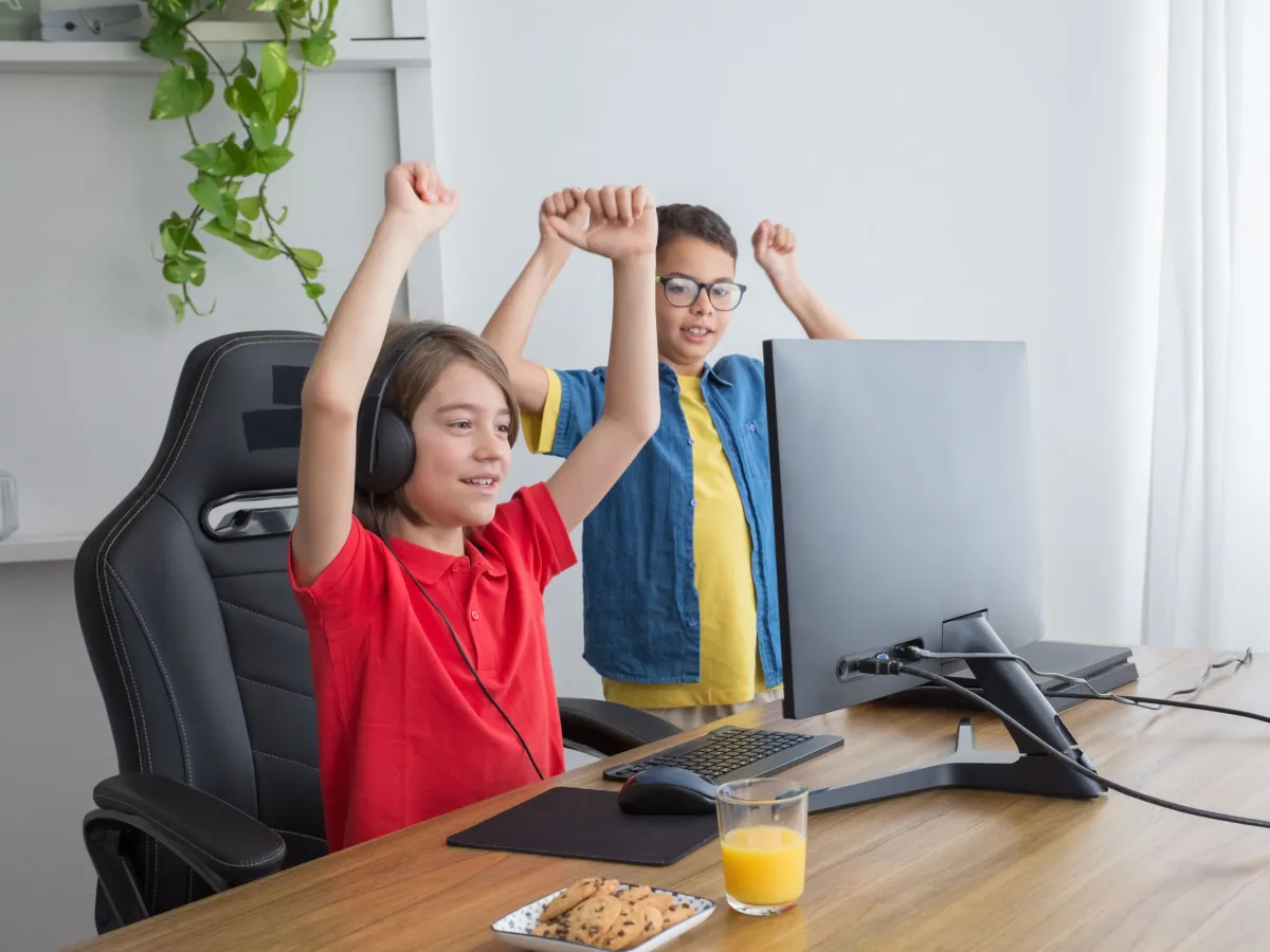 Two kids cheering with their arms up at a computer after their game works