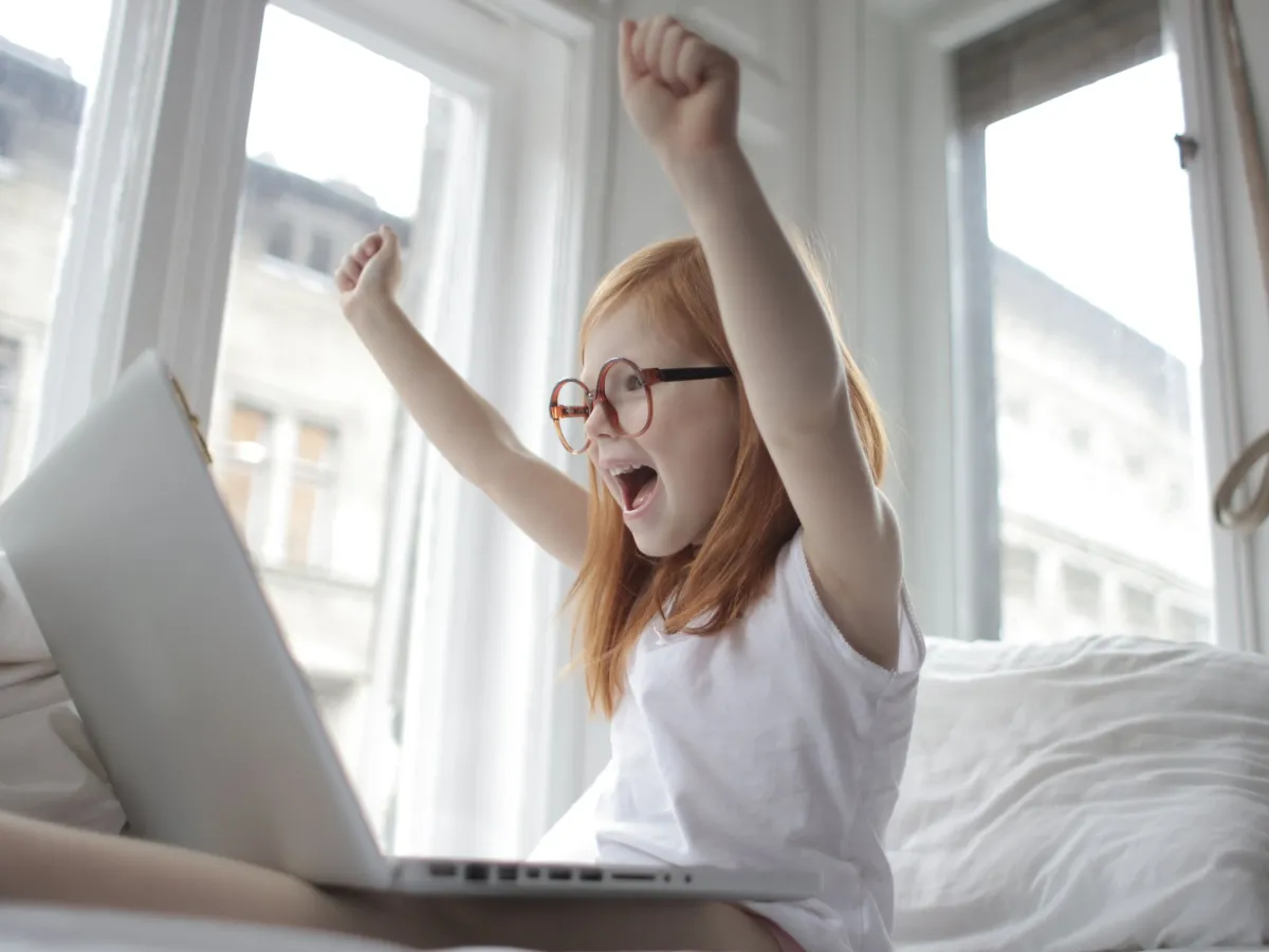 Girl in glasses cheering with both arms up in front of her laptop after her code works