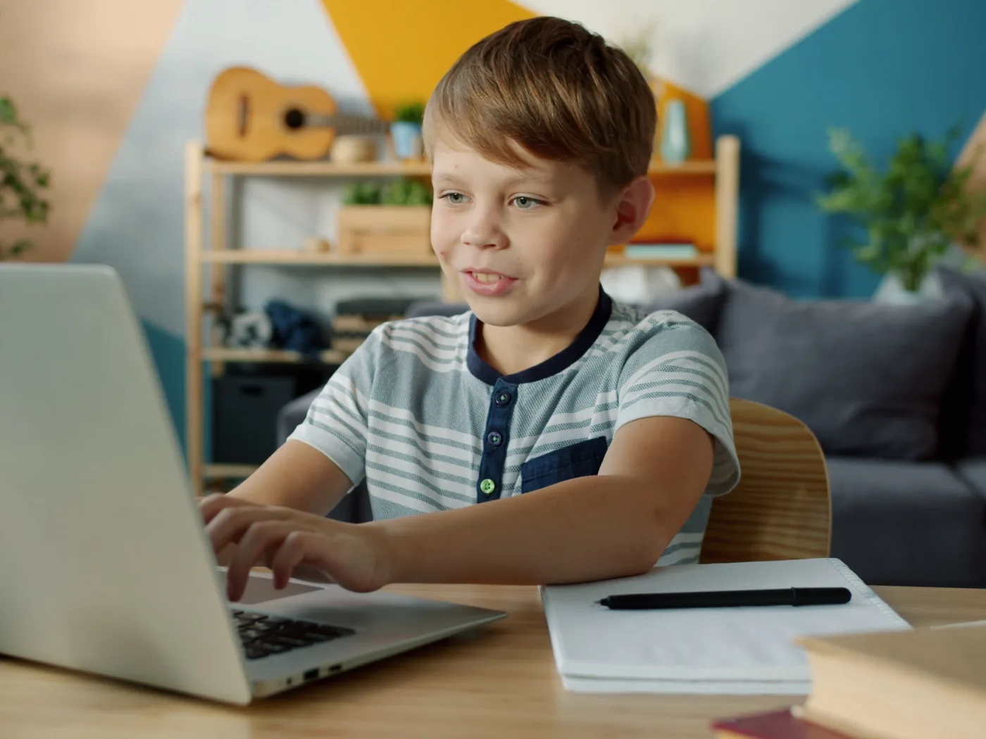 Smiling boy typing code on a laptop at a desk in a bright, colorful room