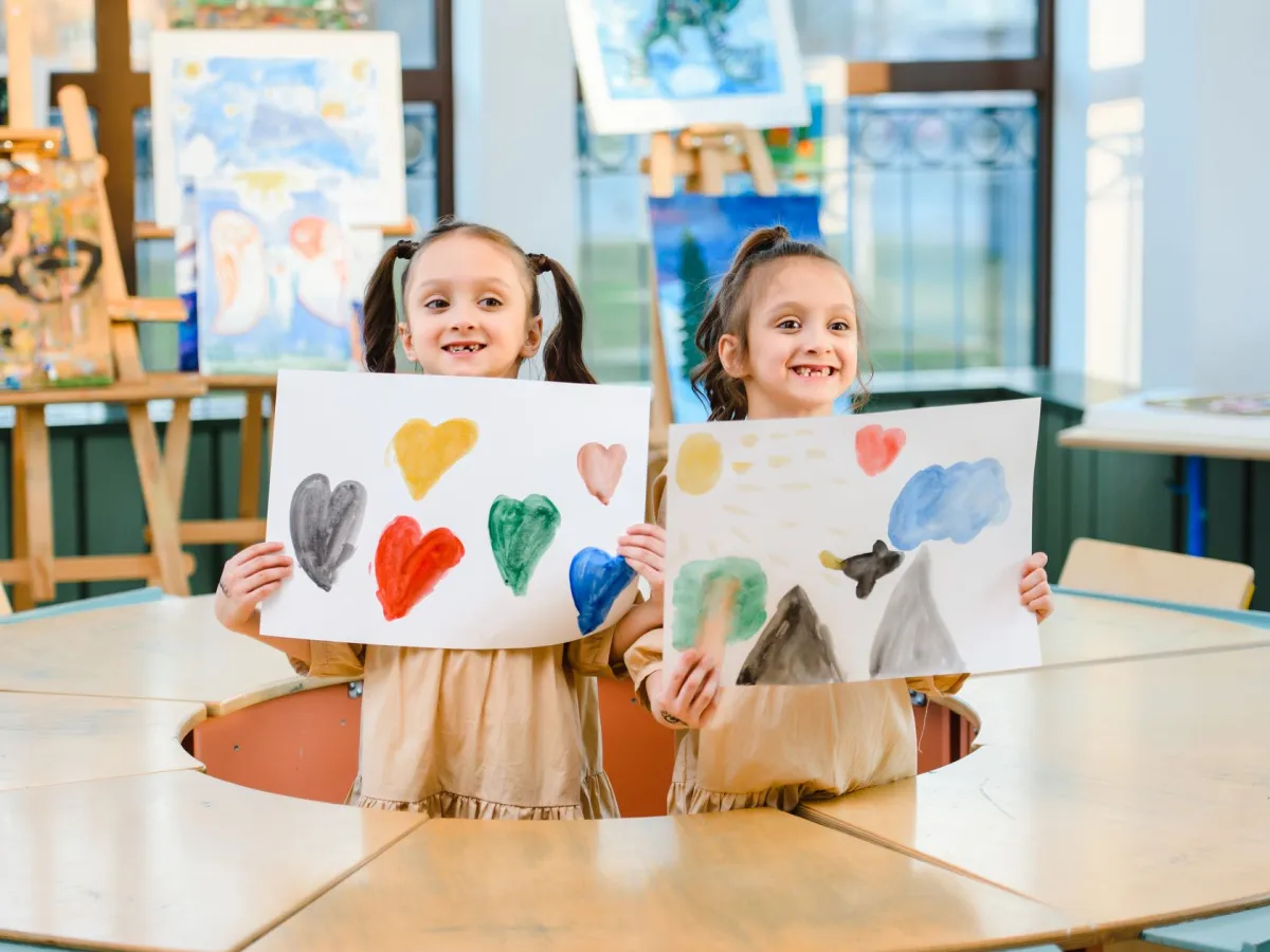 Two smiling girls proudly holding up the paintings they made